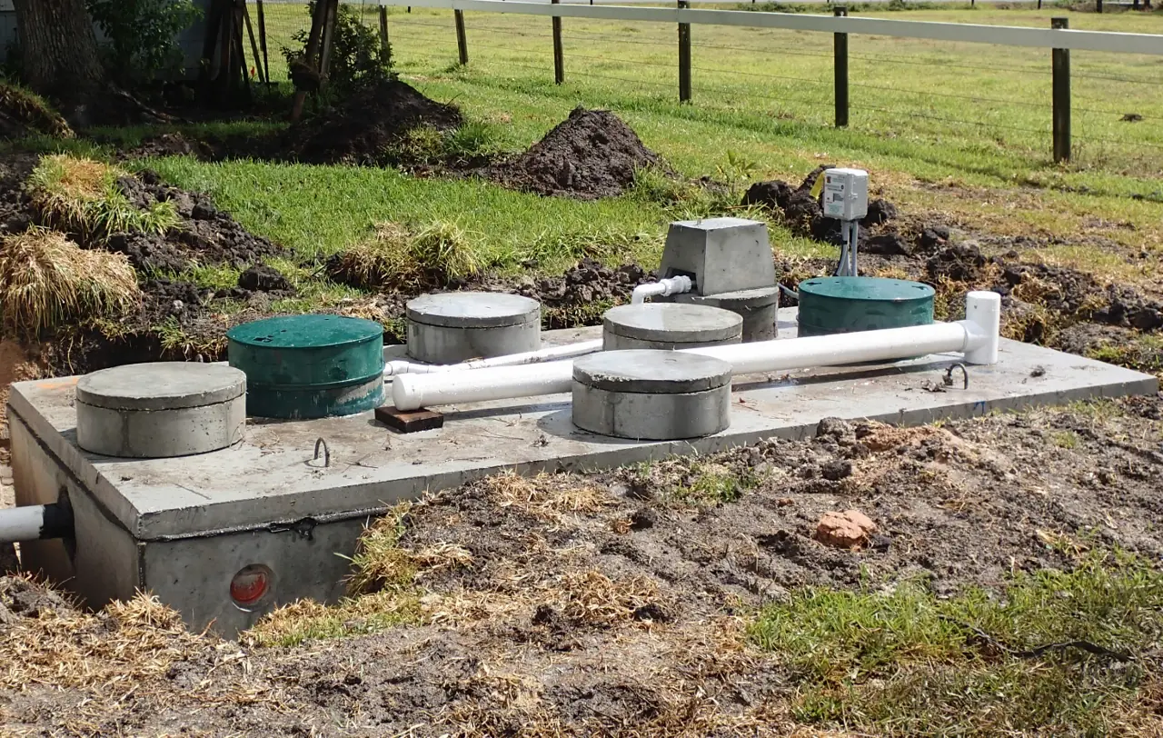 A newly installed aerobic treatment unit system: concrete tank lids and green riser caps set in fresh soil, with white PVC lines running between the tanks